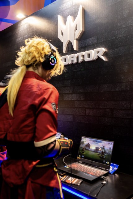 Cosplayer playing a game on a laptop at a Gamescom 2026 convention booth